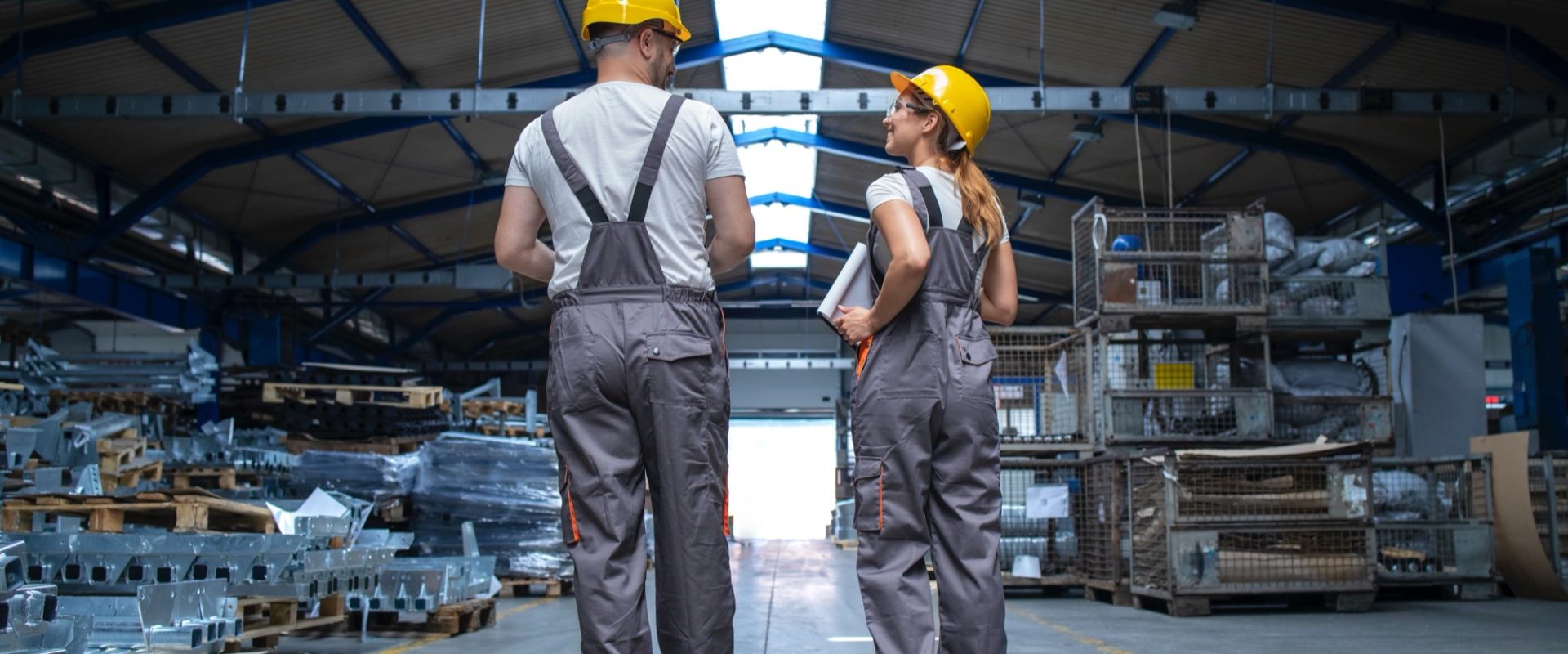 Factory workers walking through large production hall and having conversation.